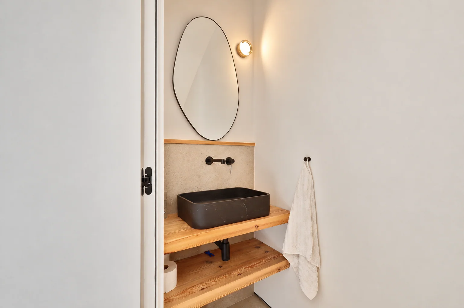 Aseo con lavabo negro, repisa de madera y espejo redondo
