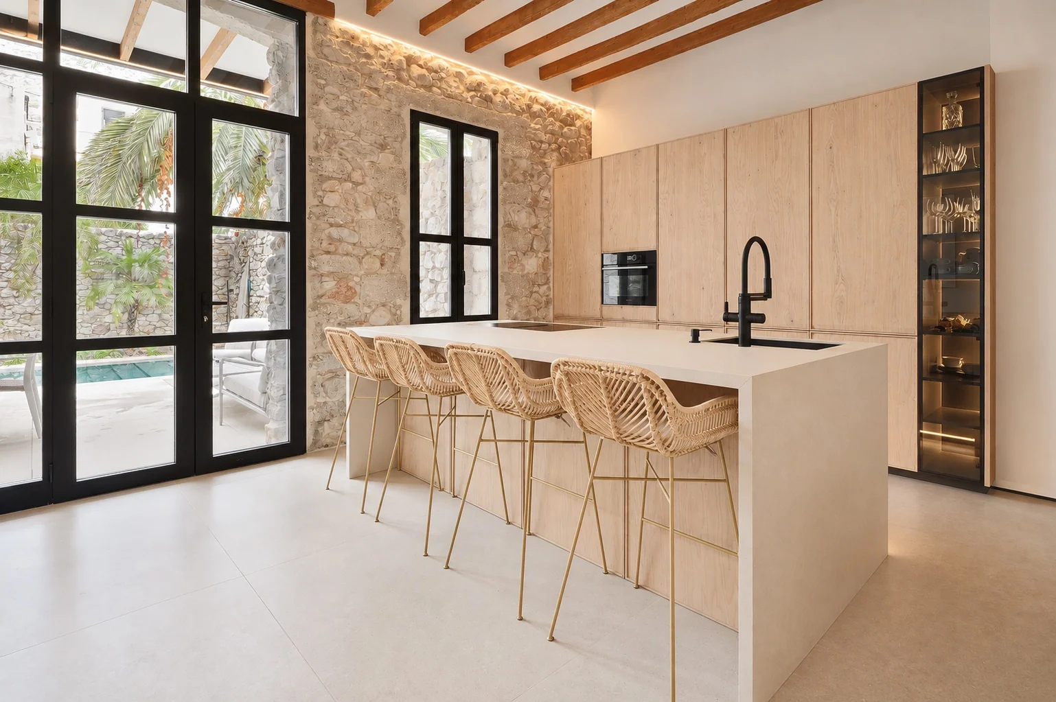 Isla de cocina con taburetes de fibras naturales, pared de piedra y armarios de madera