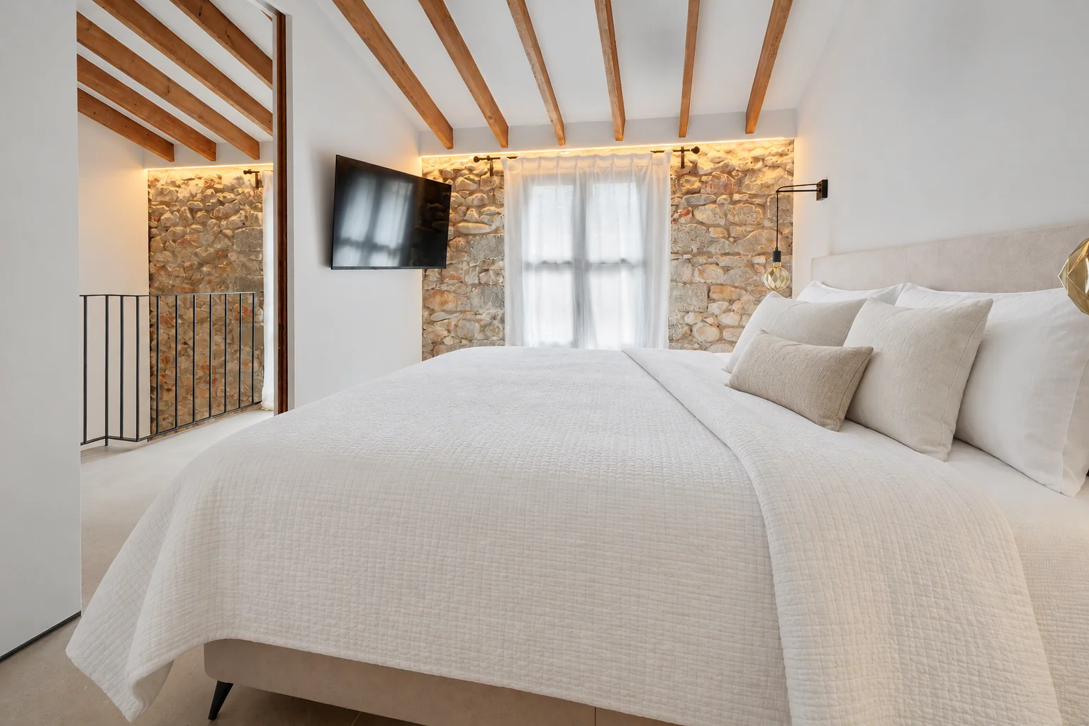 Dormitorio principal con vigas de madera, piedra vista y textiles claros