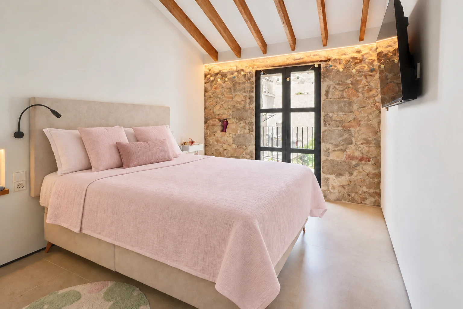 Dormitorio con textiles rosa suave, vigas y pared de piedra