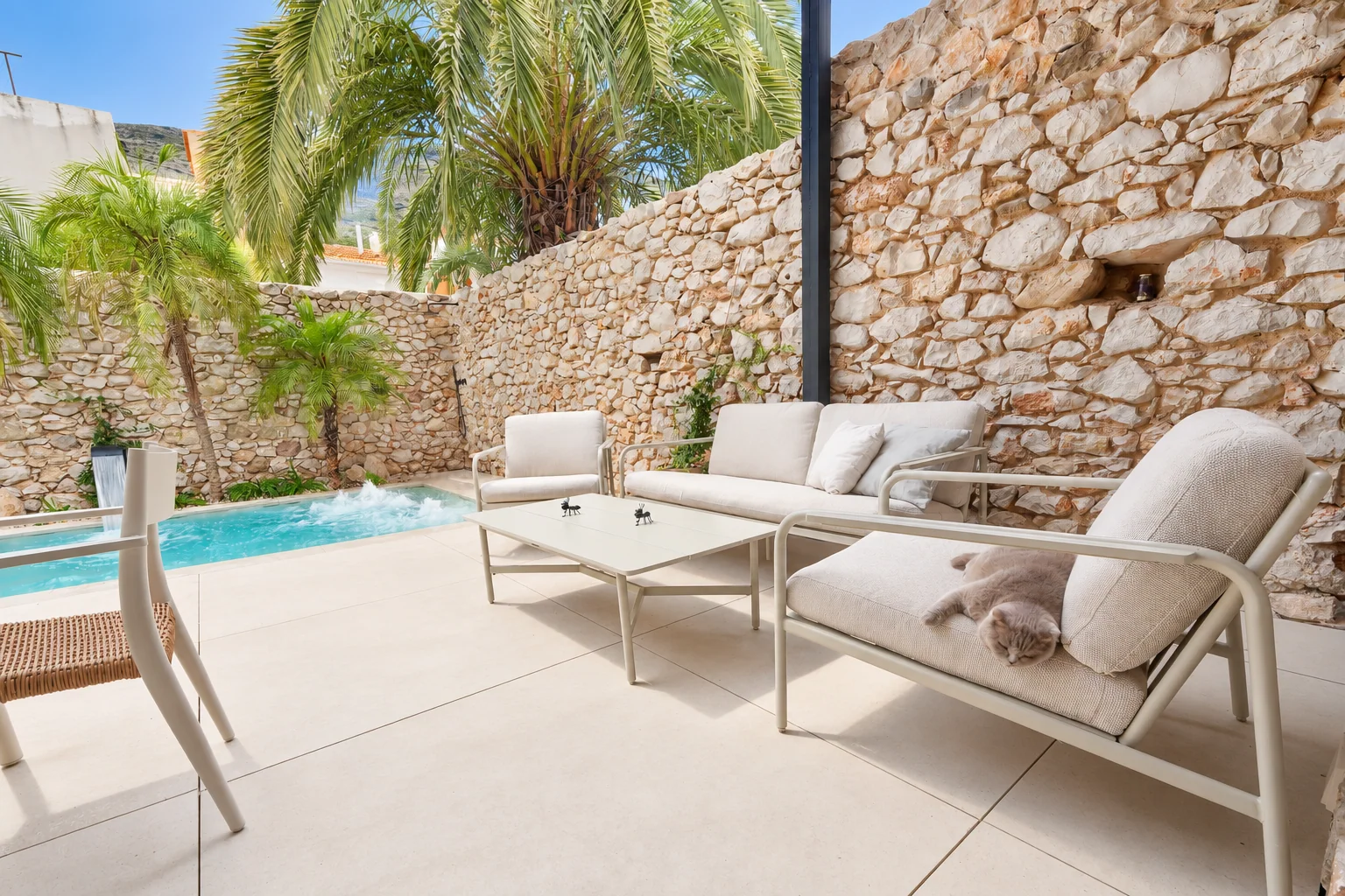 Sillones de exterior frente a la piscina y el muro de piedra